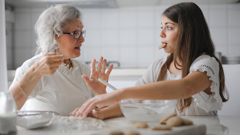 Girl eating a cookie with her grandmother at a kitchen table. Photo by Andrea Piacquadio on Pexels